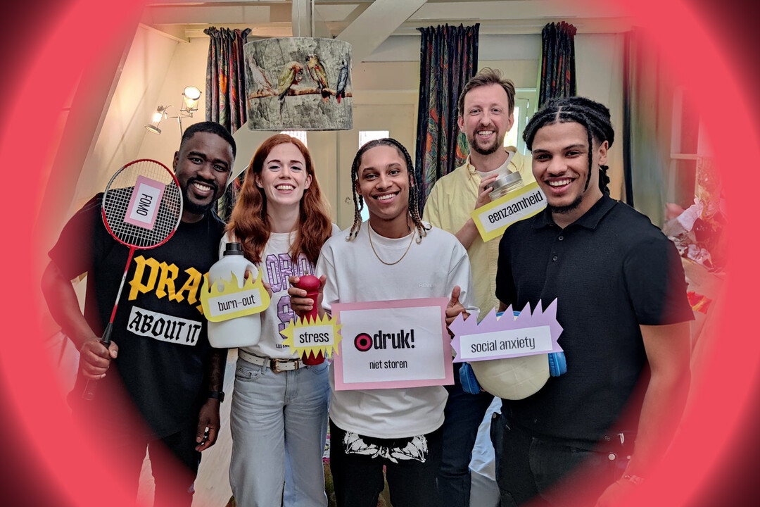 Vijf personen kijken lachend naar de camera en houden bordjes vast met gevoels erop