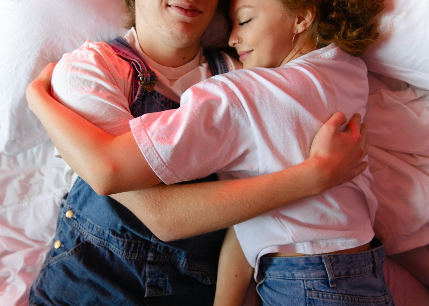 Een stel ligt ontspannen bovenop bed en zij omhelzen elkaar liefdevol.