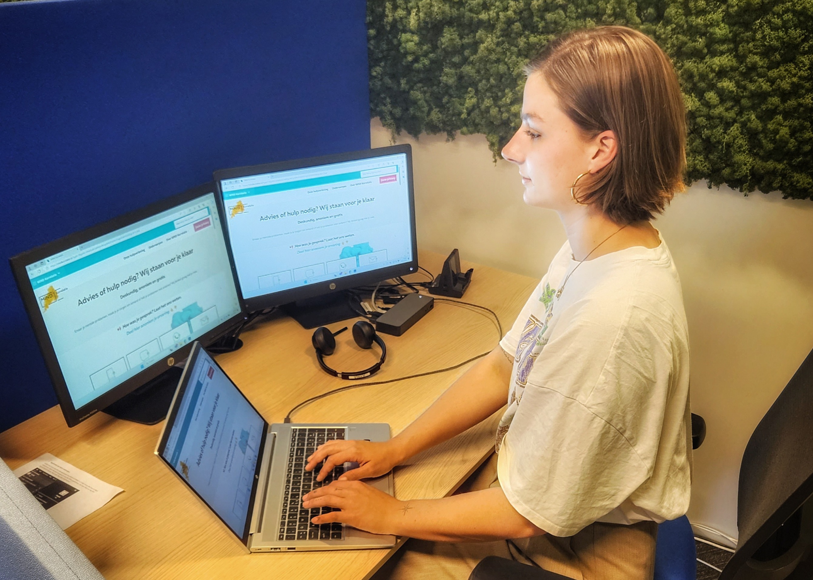 Een vrouw werkt geconcentreerd achter haar laptop en monitoren in het kantoor van de MIND Hulplijn