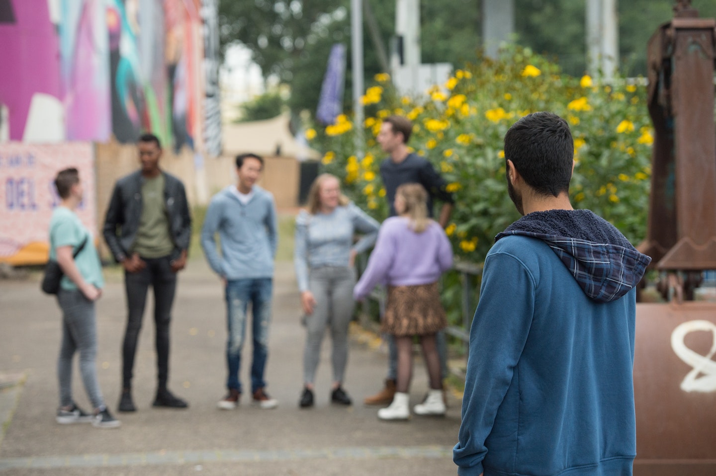 Een persoon staat alleen buiten en kijkt van afstand naar een kletsende vriendengroep