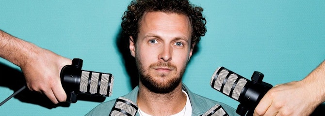 Tim  Senders kijkt zelfverzekerd in de camera met onder zijn gezicht microfoons