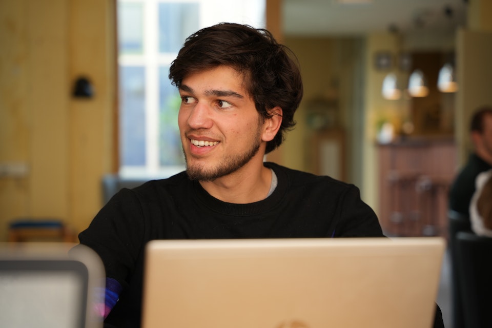 Lachende man die als vrijwilliger voor @ease werkt achter zijn laptop op een gezellig plek