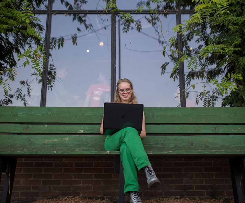 Vrouw werkt rustig buiten op een bankje met haar laptop, omringd door groen
