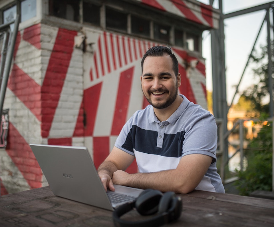 Lachende man die buiten op zijn laptop werkt
