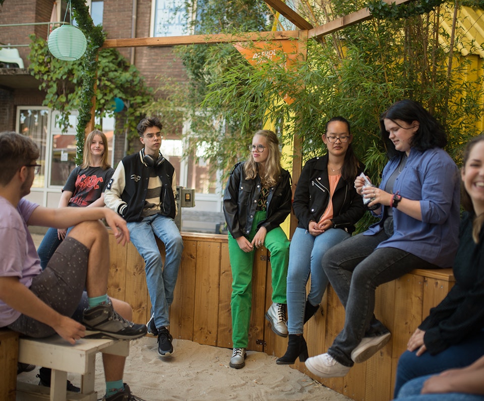 Een groep jongeren die met elkaar gezellig buiten zit