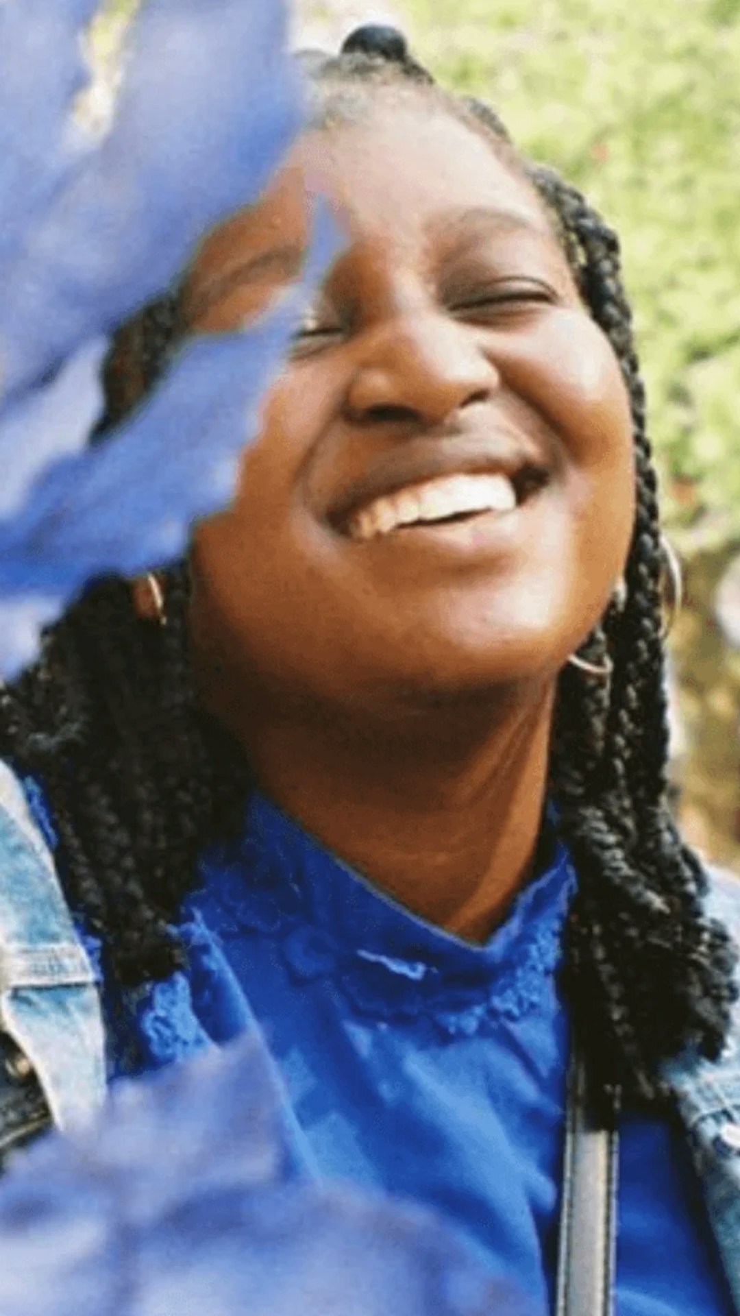 Nishaya staat lachend buiten naast een plant