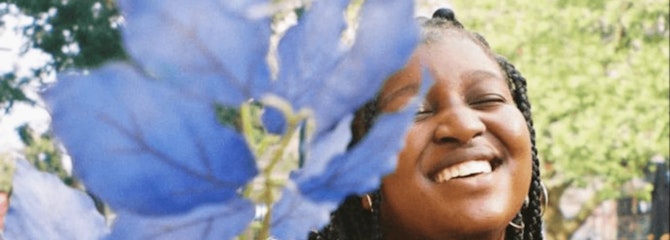 Nishaya staat lachend buiten naast een plant