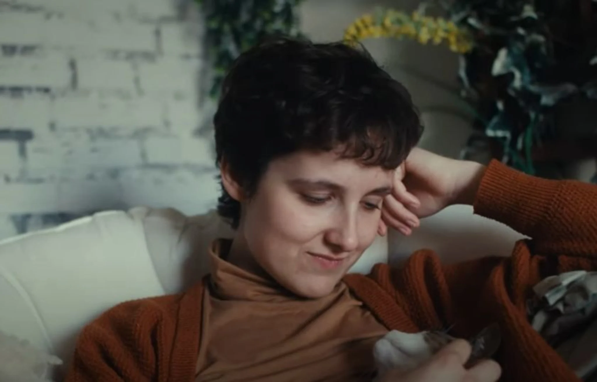 Sanja zit op de bank met haar hand onder haar hoofd, terwijl ze de kat bij op haar schoot aait