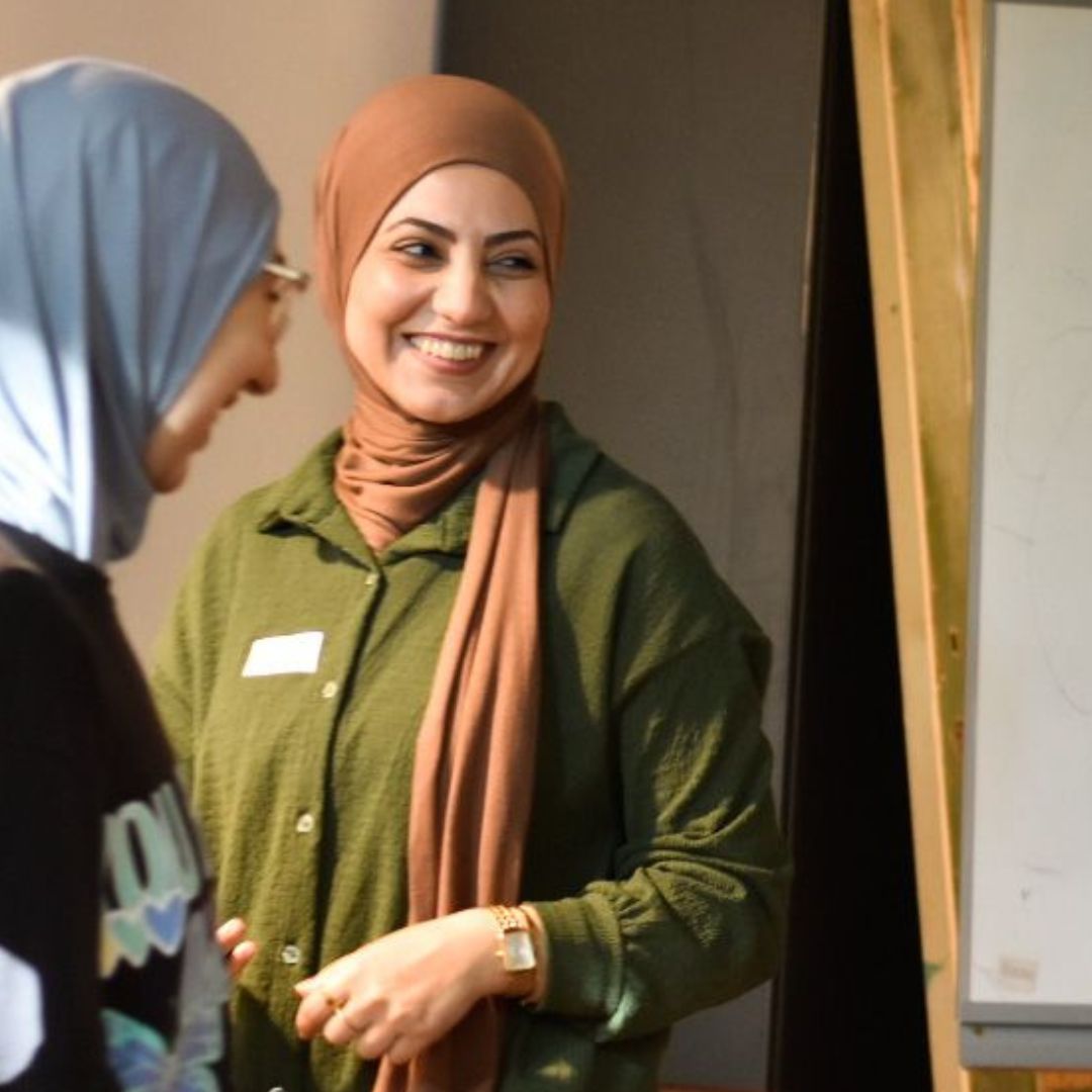 Halime en een vriedin staan voor een flipover en kijken lachend opzij