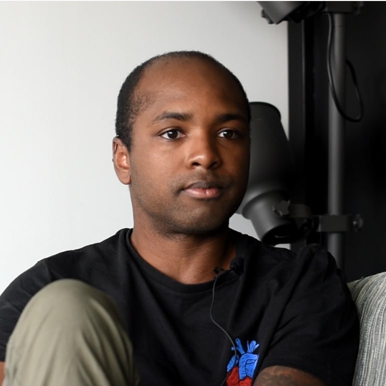 Elwin denkt na, zit op een bank met zijn knie omhoog en kijkt in de camera