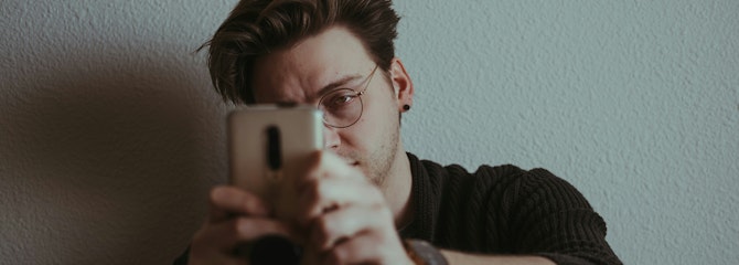 Een jongen zit tegen de muur en kijkt op zijn telefoon.
