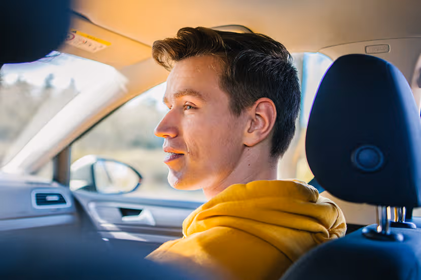 Julius zit als bijrijder in een auto en kijkt naar de bestuurder.