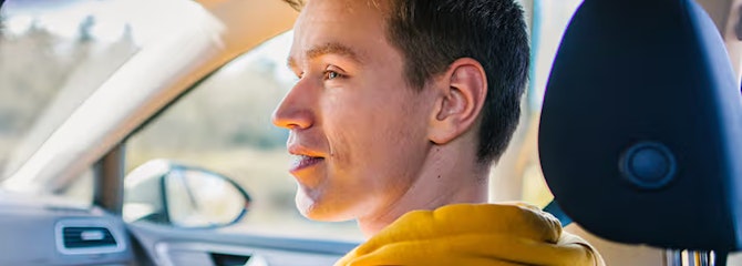 Julius zit als bijrijder in een auto en kijkt naar de bestuurder.
