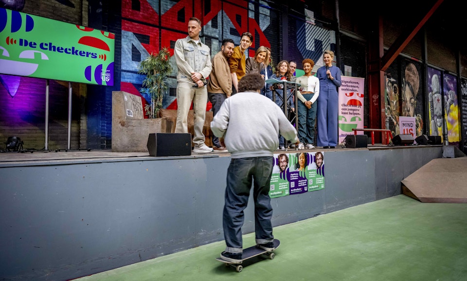 Een jongen op een skateboard tijdens de lancering van De Checkers, met daarachter onder andere Koning Máxima en Giel de Winter.