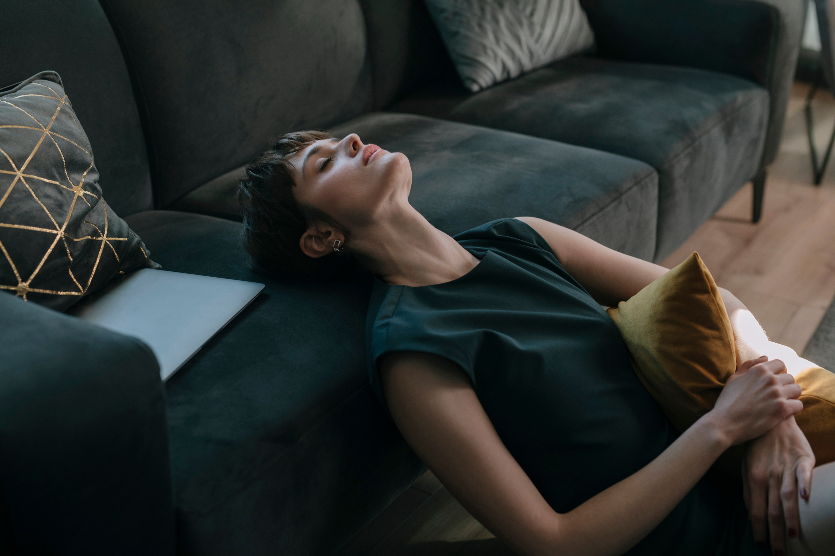 Vrouw zit rustig op de grond, naast een bank en leunt hier achterover tegenaan