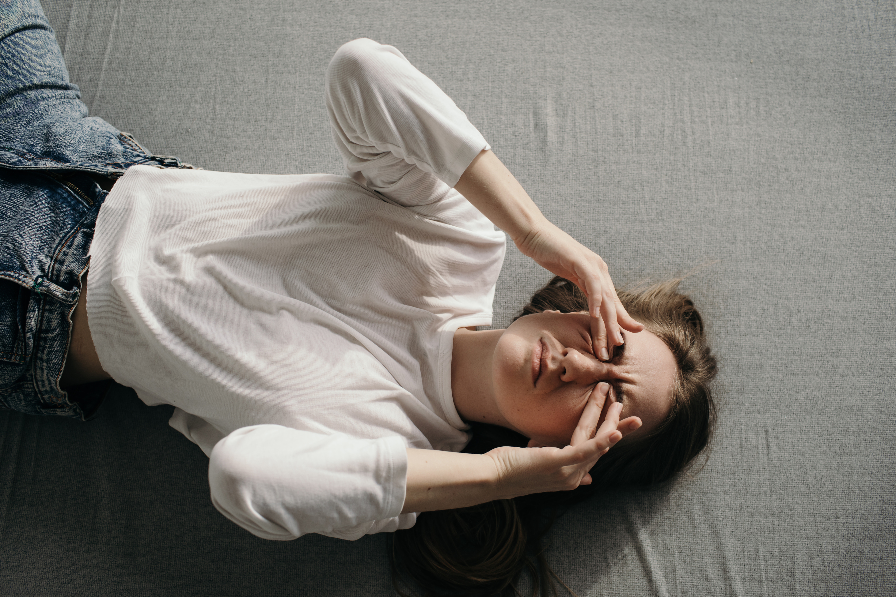 Gestresste jonge vrouw ligt op de grond met haar handen voor haar ogen.