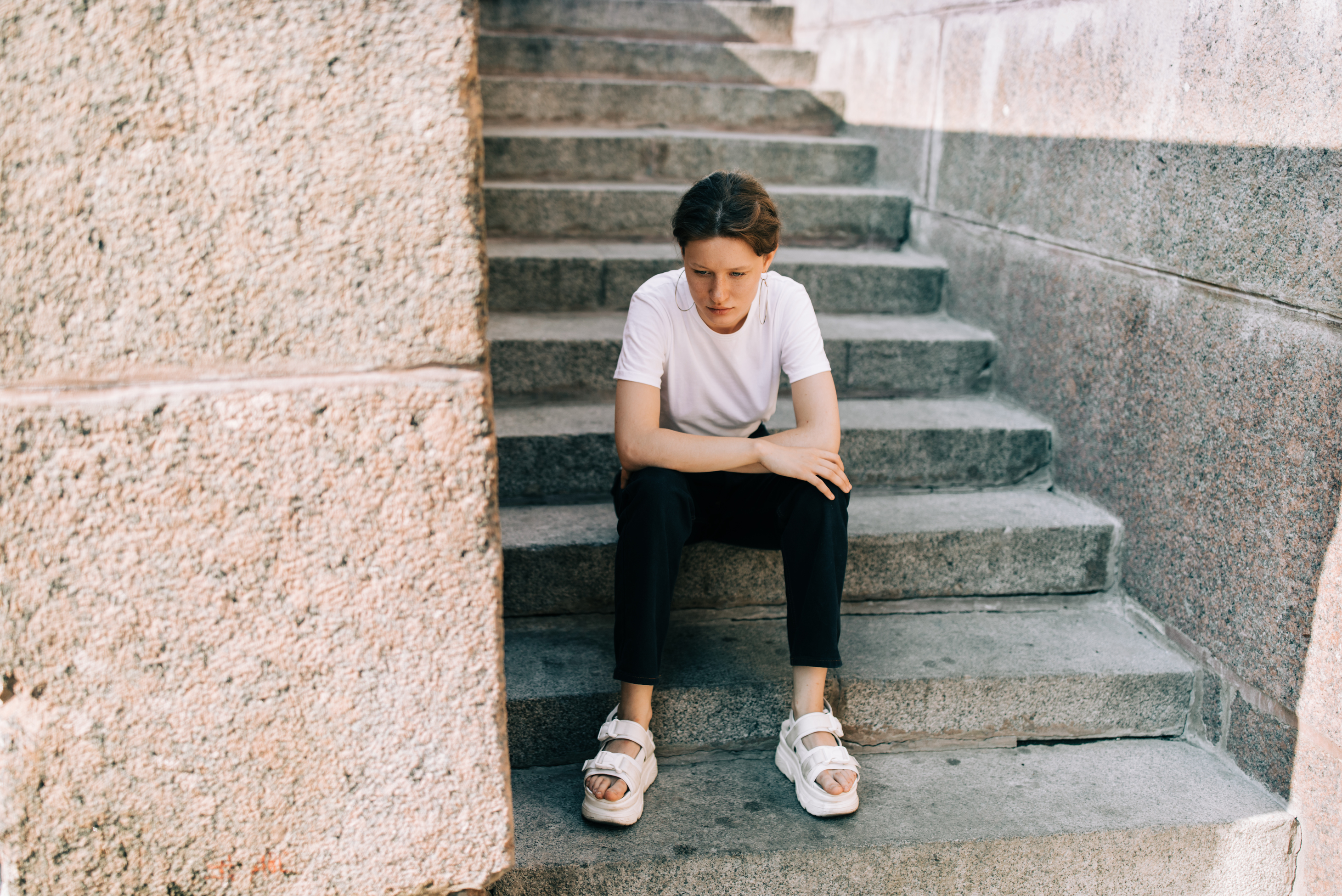 Persoon zit voorover met armen over elkaar op een trap buiten