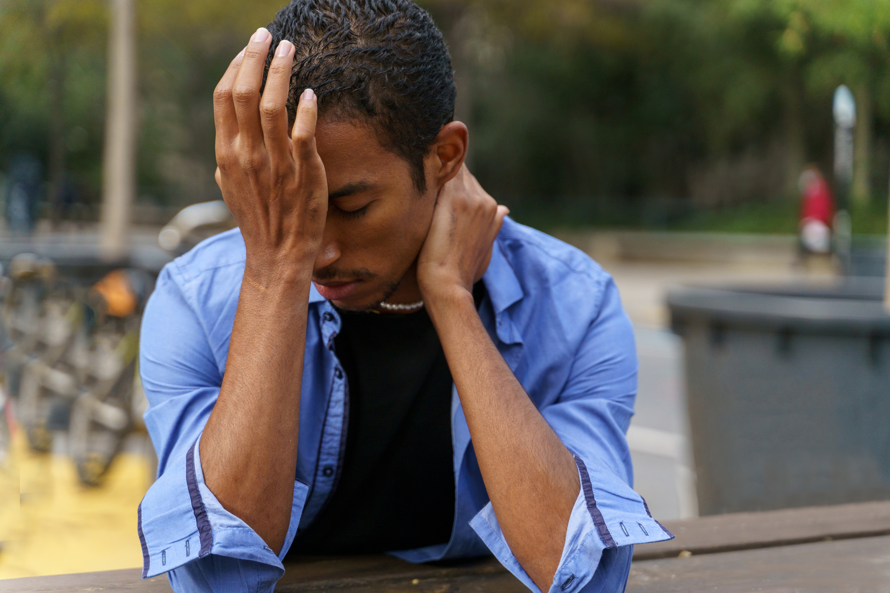 Een jongeman zit buiten, zichtbaar in paniek en houdt zijn hoofd vast