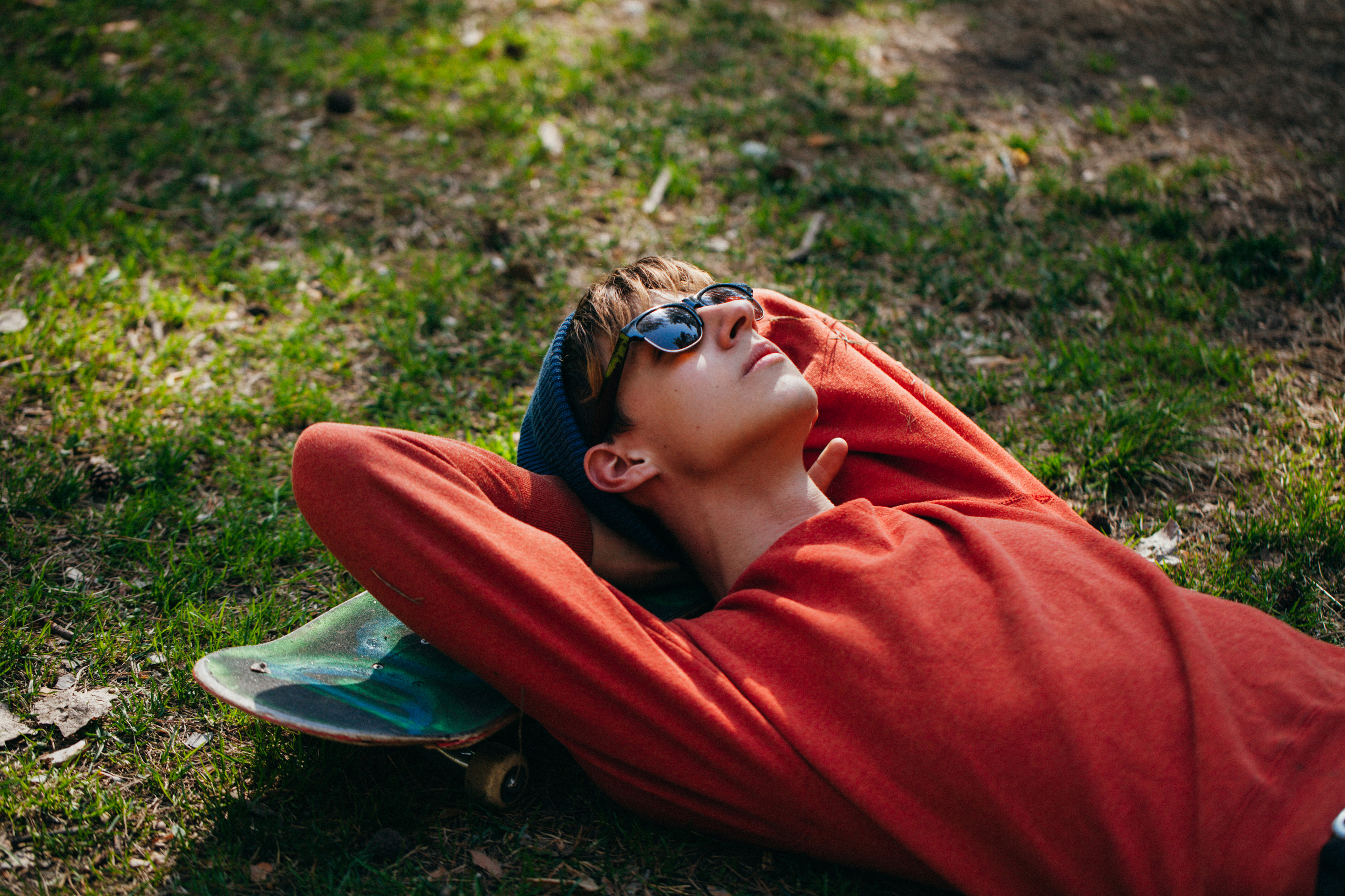 Man ligt relaxed in een park met zijn hoofd op zijn skatebord op een zonnige dag.