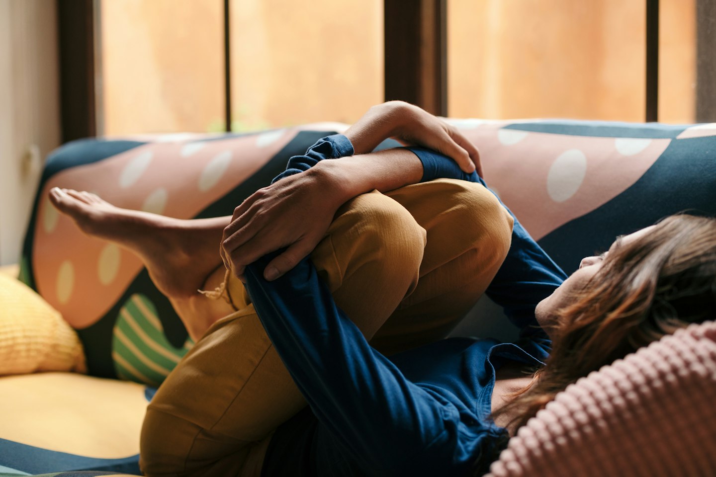 Vrouw ligt ontspannen op de bank met haar armen om haar benen en staart naar voor zich uit