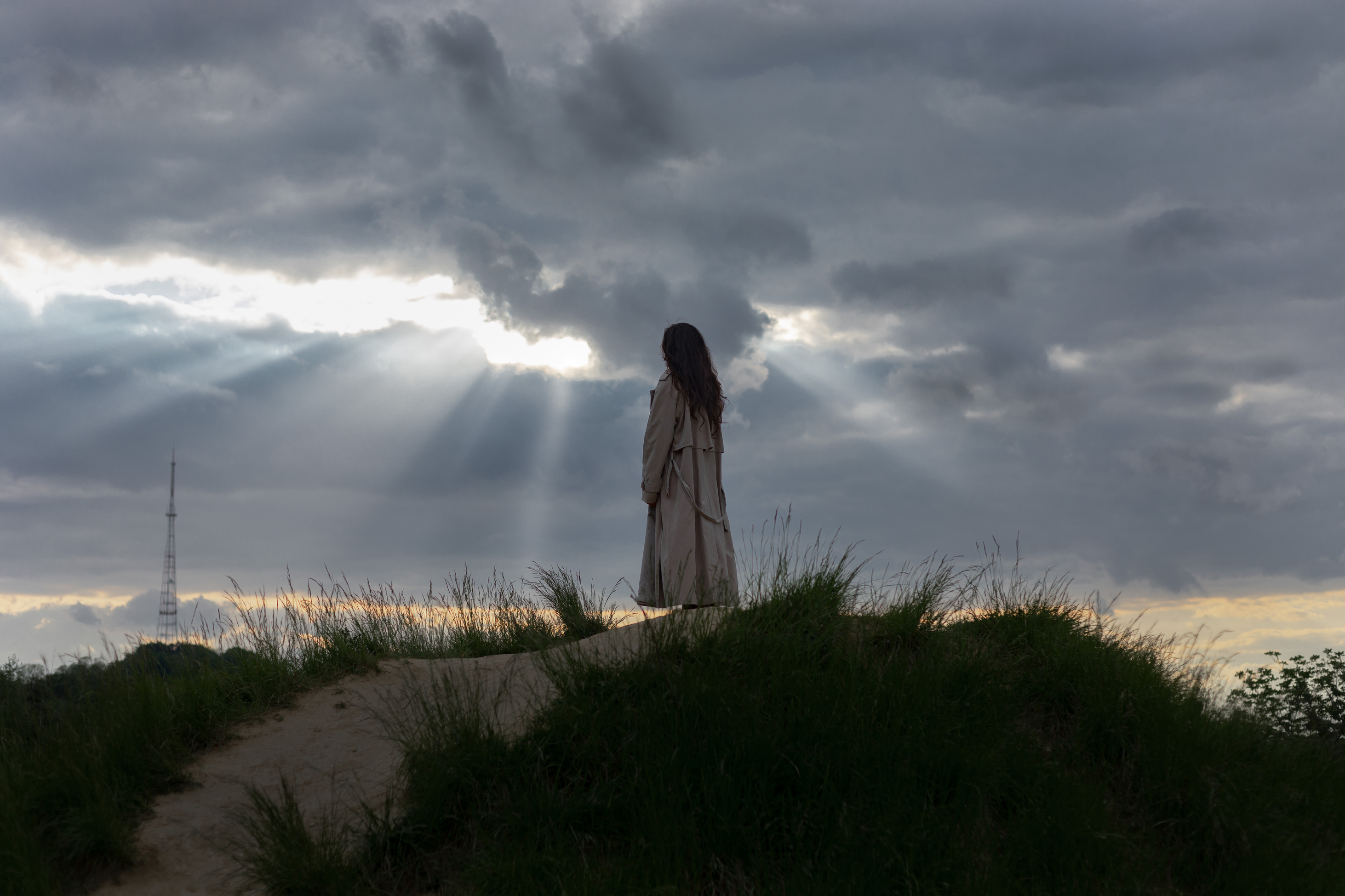 Vrouw staat op een duin onder een indrukwekkende lucht met zonnestralen, die door de wolken breken