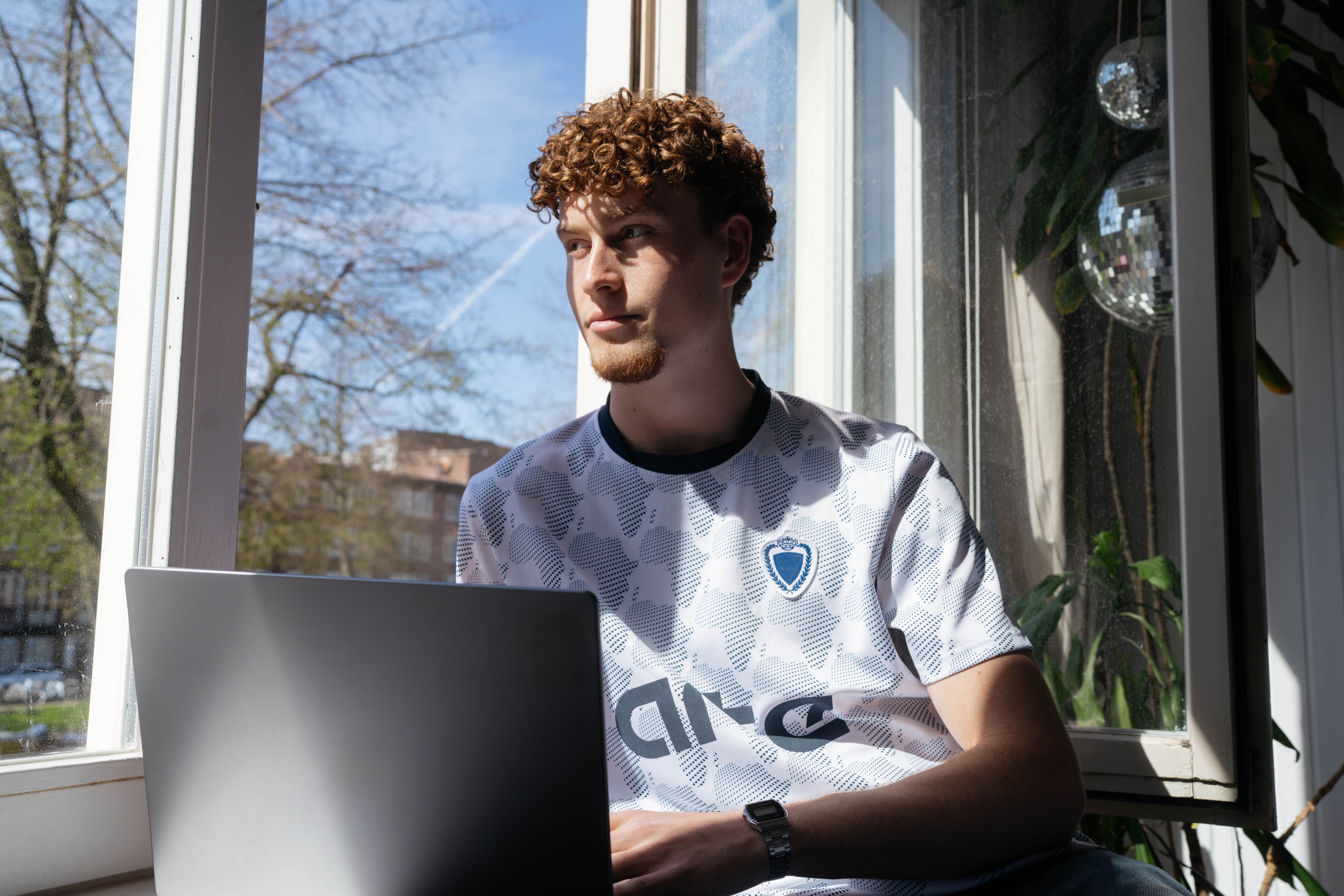 Man zit op een zonnige dag alleen bij een raam te werken op zijn laptop en staart naar buiten