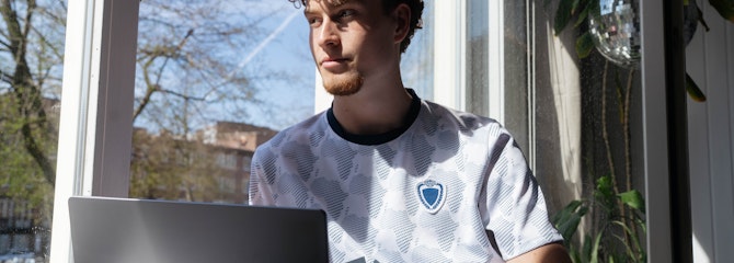 Man zit op een zonnige dag alleen bij een raam te werken op zijn laptop en staart naar buiten