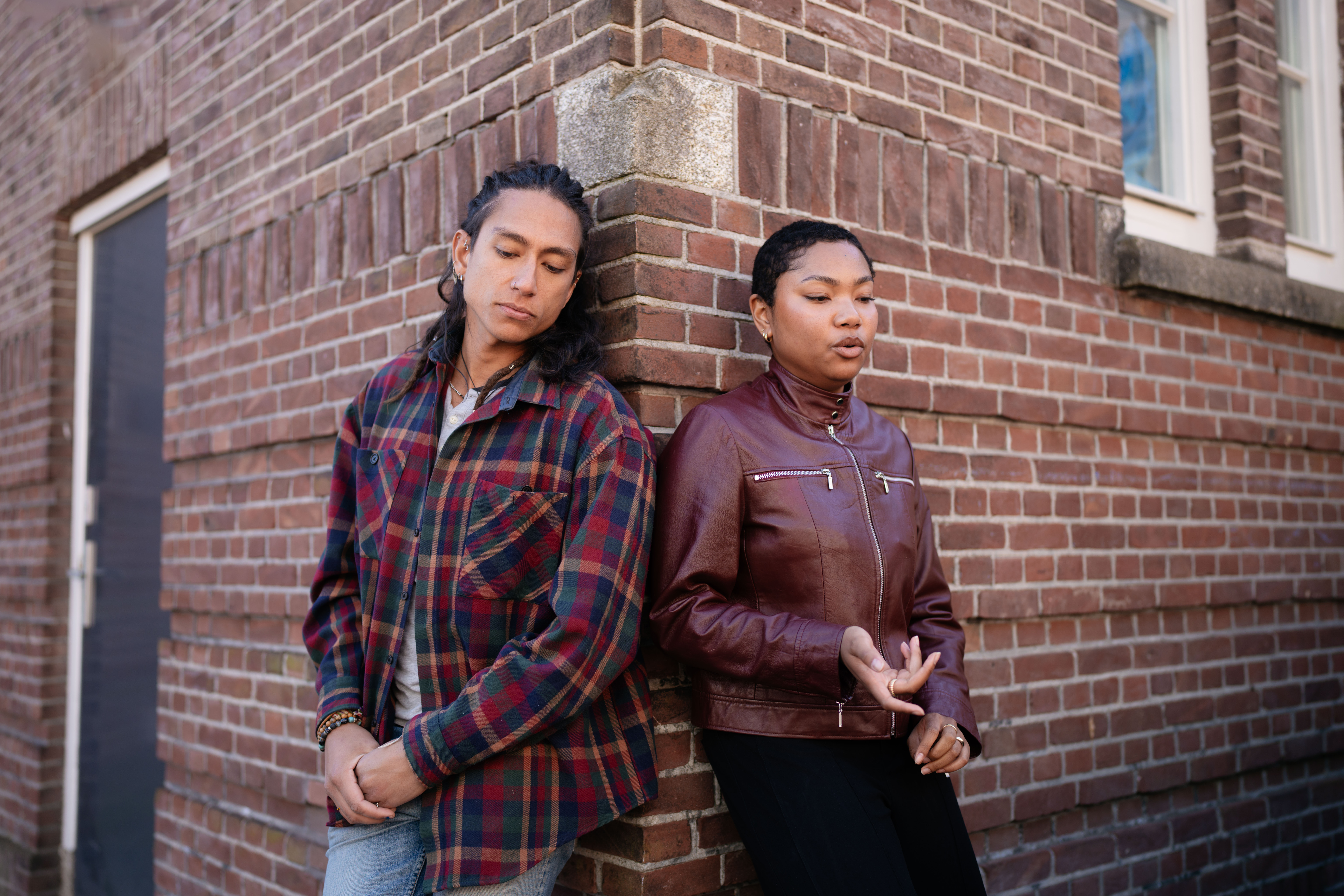 Twee personen voeren een gesprek leunend tegen een bakstenen gebouw