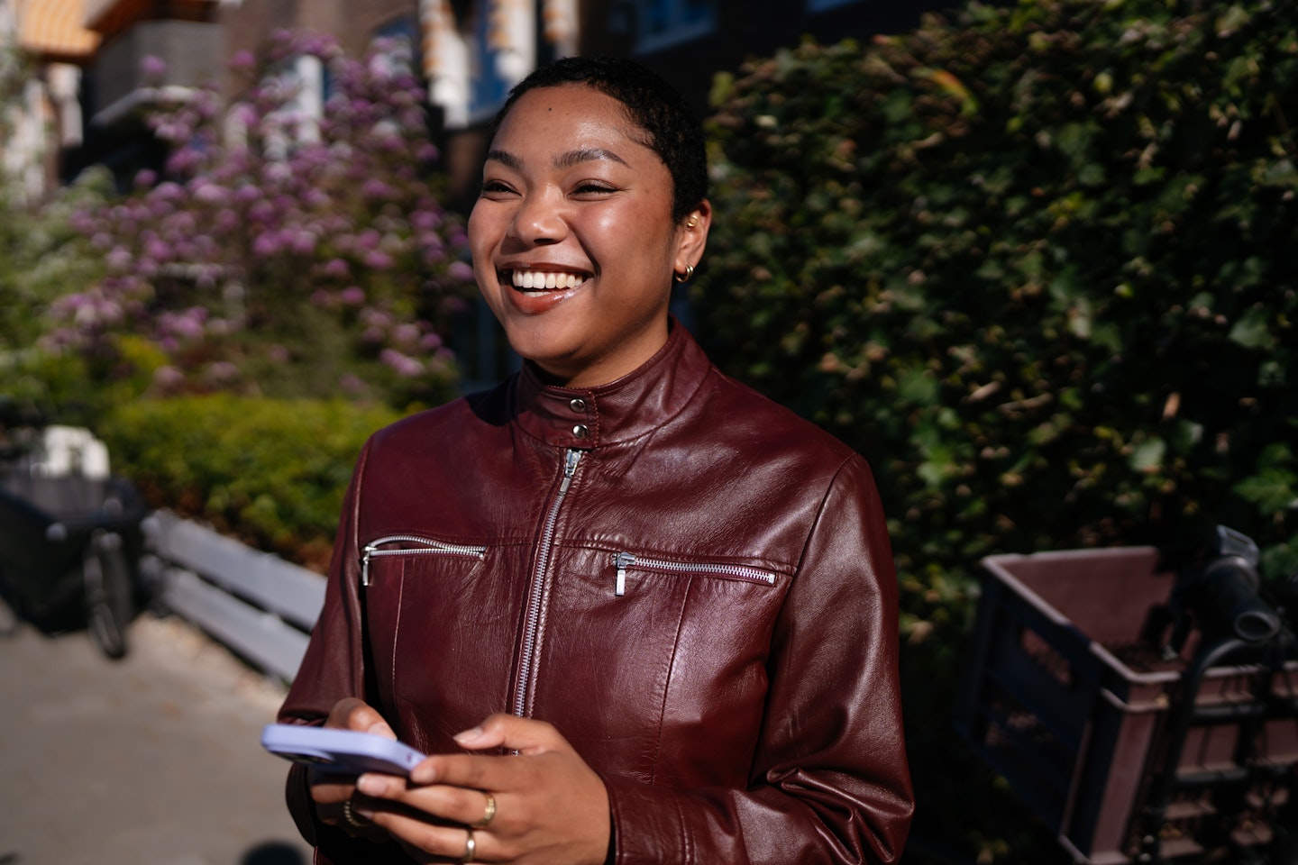 Een vrolijke jonge vrouw staat buiten in de zon en kijkt op van haar telefoon