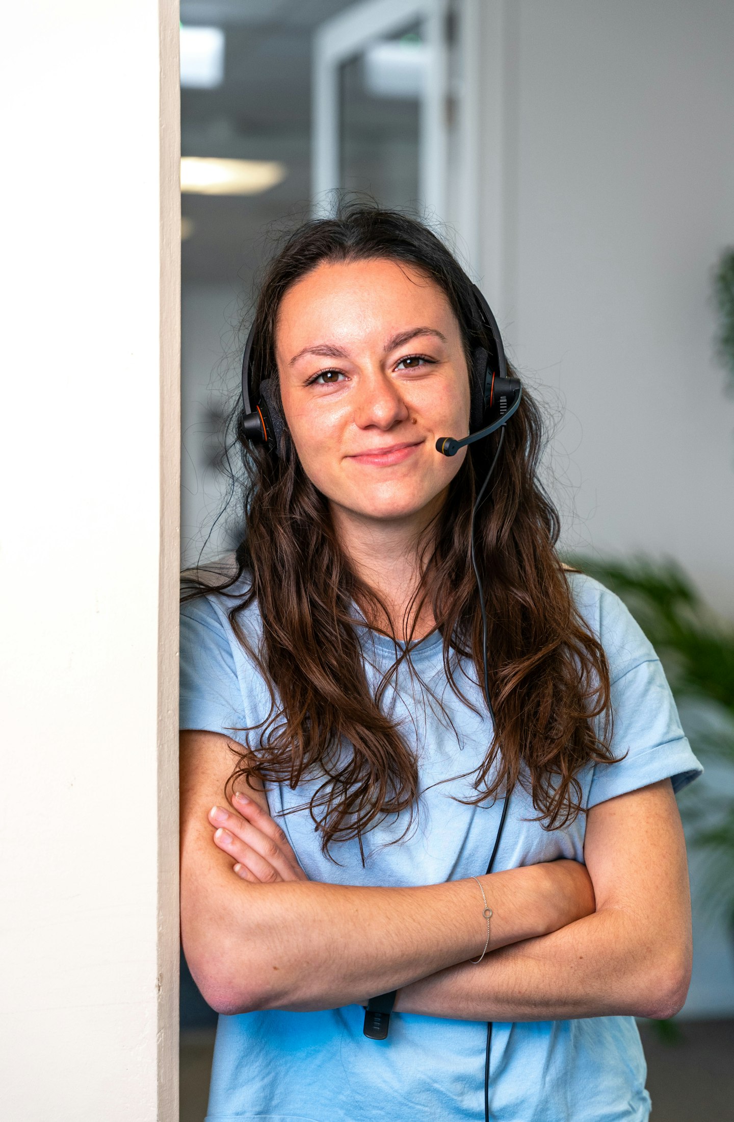 jonge vrouw met headset op staat lachend tegen een deur geleund