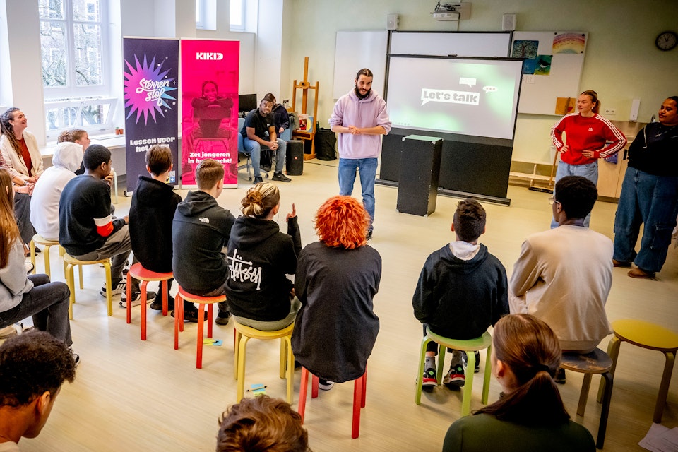 Jongeman van Stichting Kikid geeft presentatie voor groep scholieren