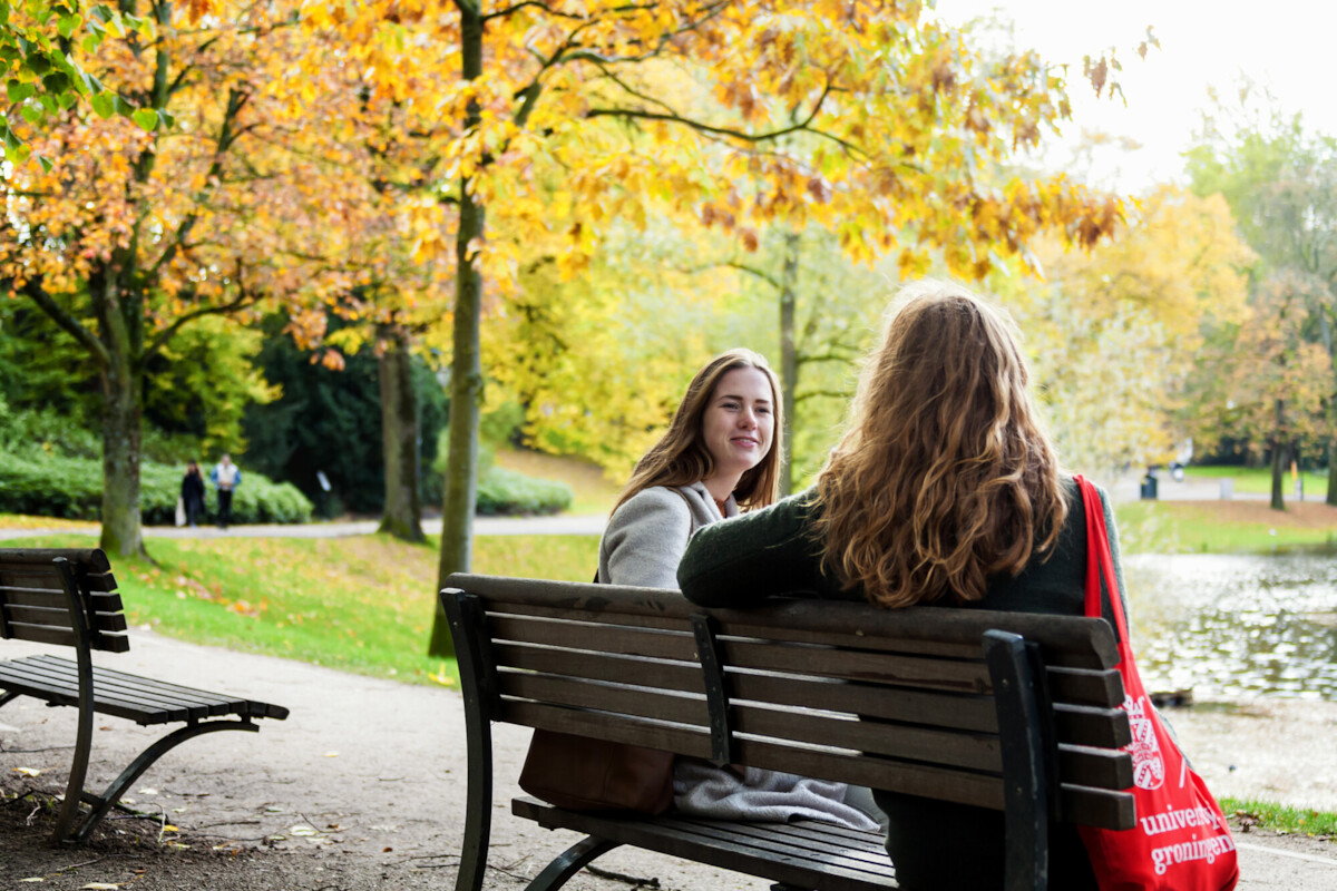 twee jonge vrouwelijke studenten op een bankje in een park in de herfst