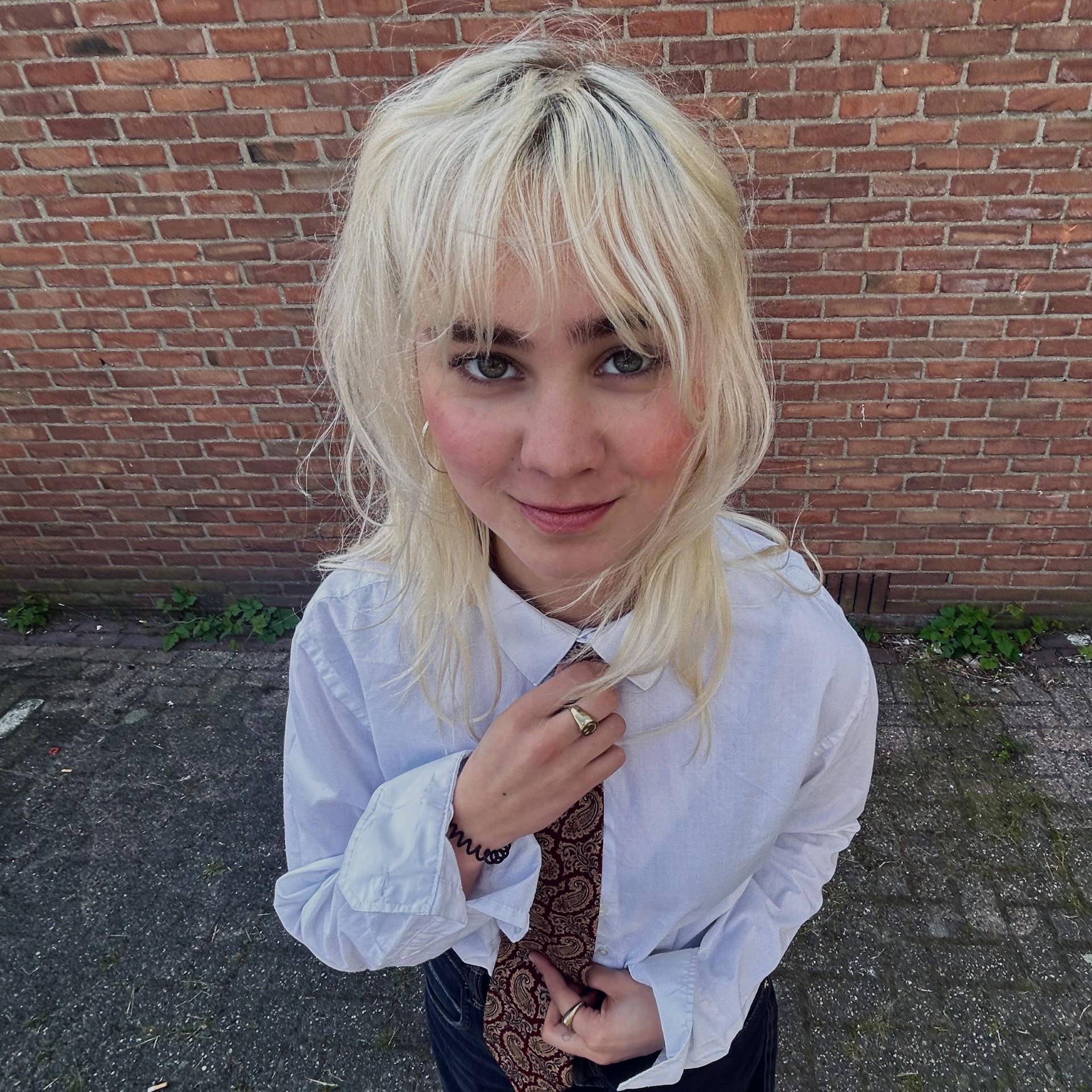 Ella staat voor een muur en kijkt recht in de camera.