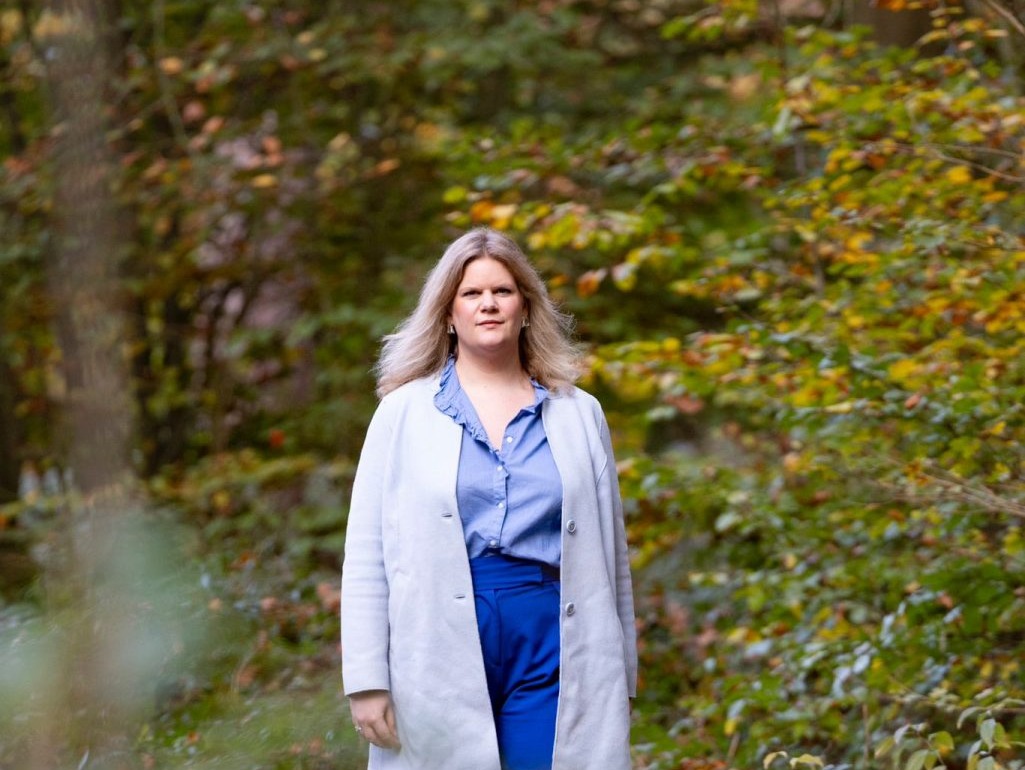 Jonge blonde vrouw in blauwe outfit wandelt in het bos in de vroege herfst