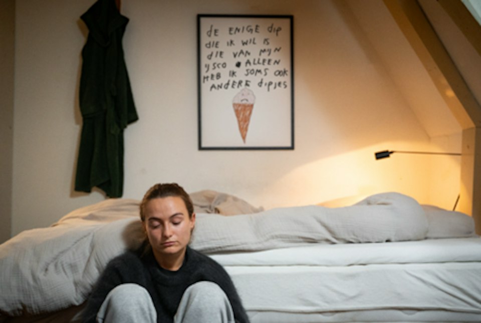 Meisje zit op de grond tegen haar bed met kunstwerk over dip aan de muur