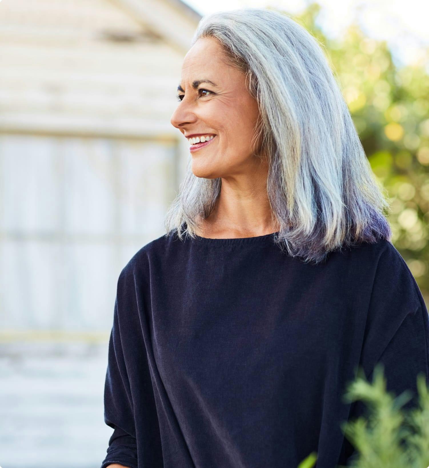 Middle-aged woman with long silver hair smiling, wearing black top, outdoor setting