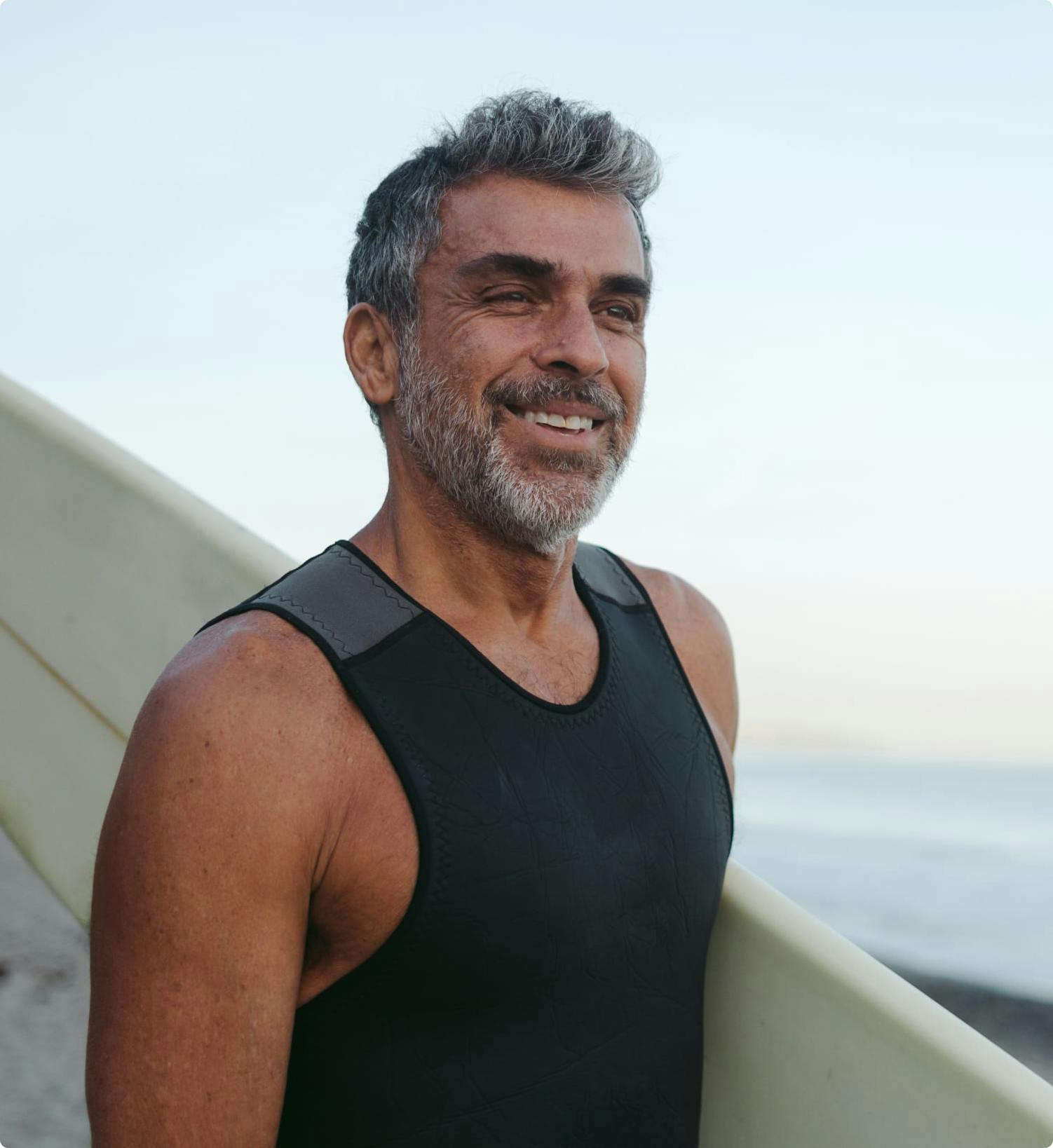 Man with with greyish hair and beard, holding a surfboard