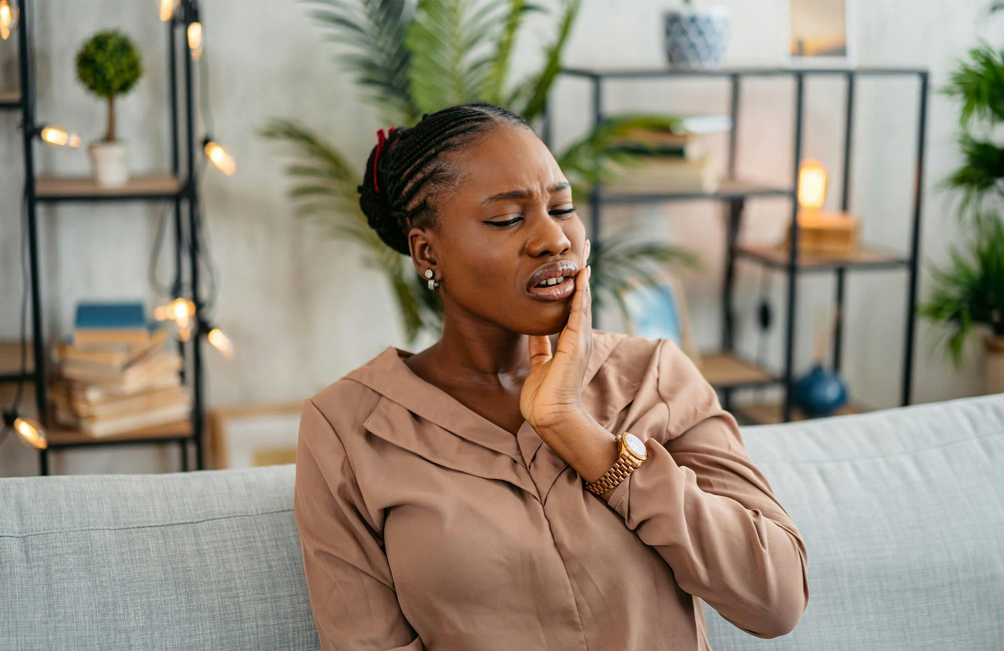 woman sitting down and touching her jaw showing shes in pain
