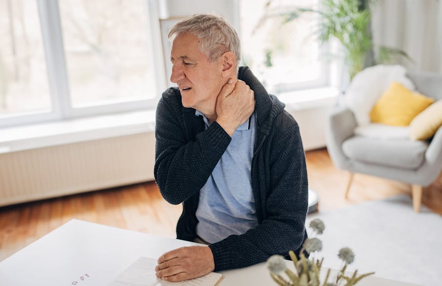 older man sitting down holding his neck showing hes in pain
