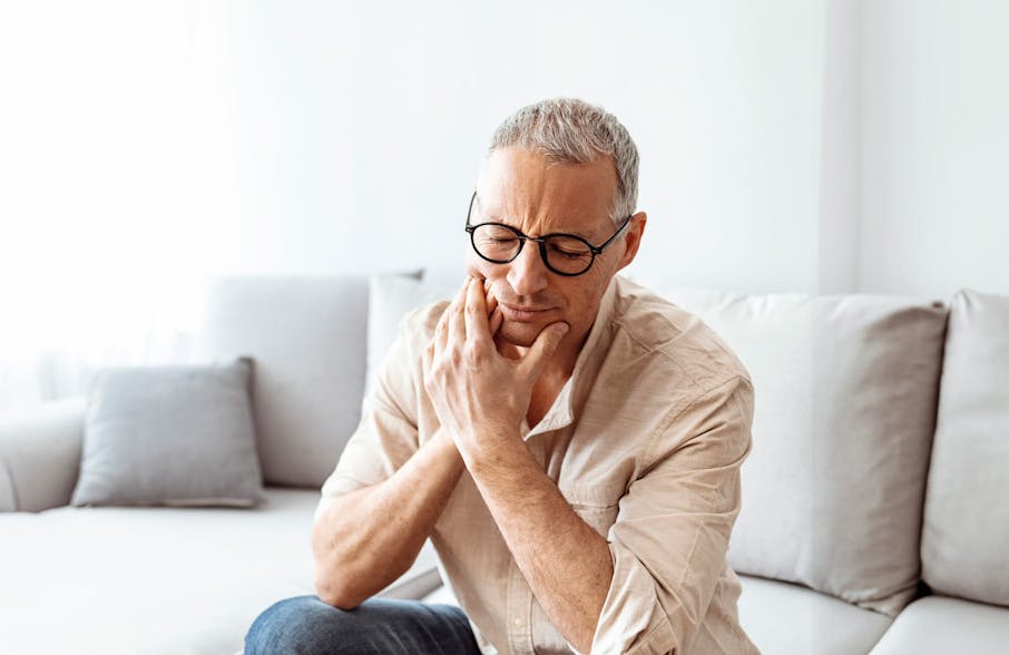 man sitting on couch touching side of face
