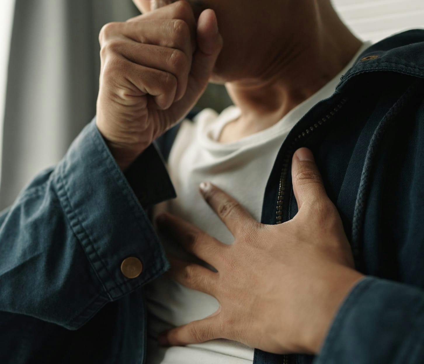person with fist in front of their mouth and their hand on their chest