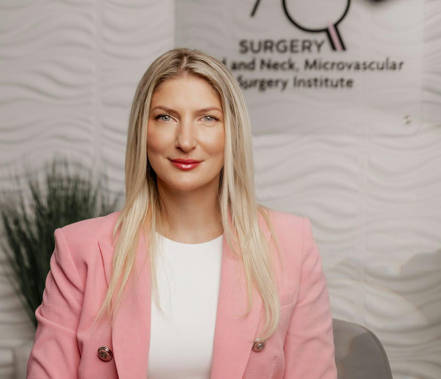 Dr. Quimby in pink suit sitting infront of AQ Surgery logo