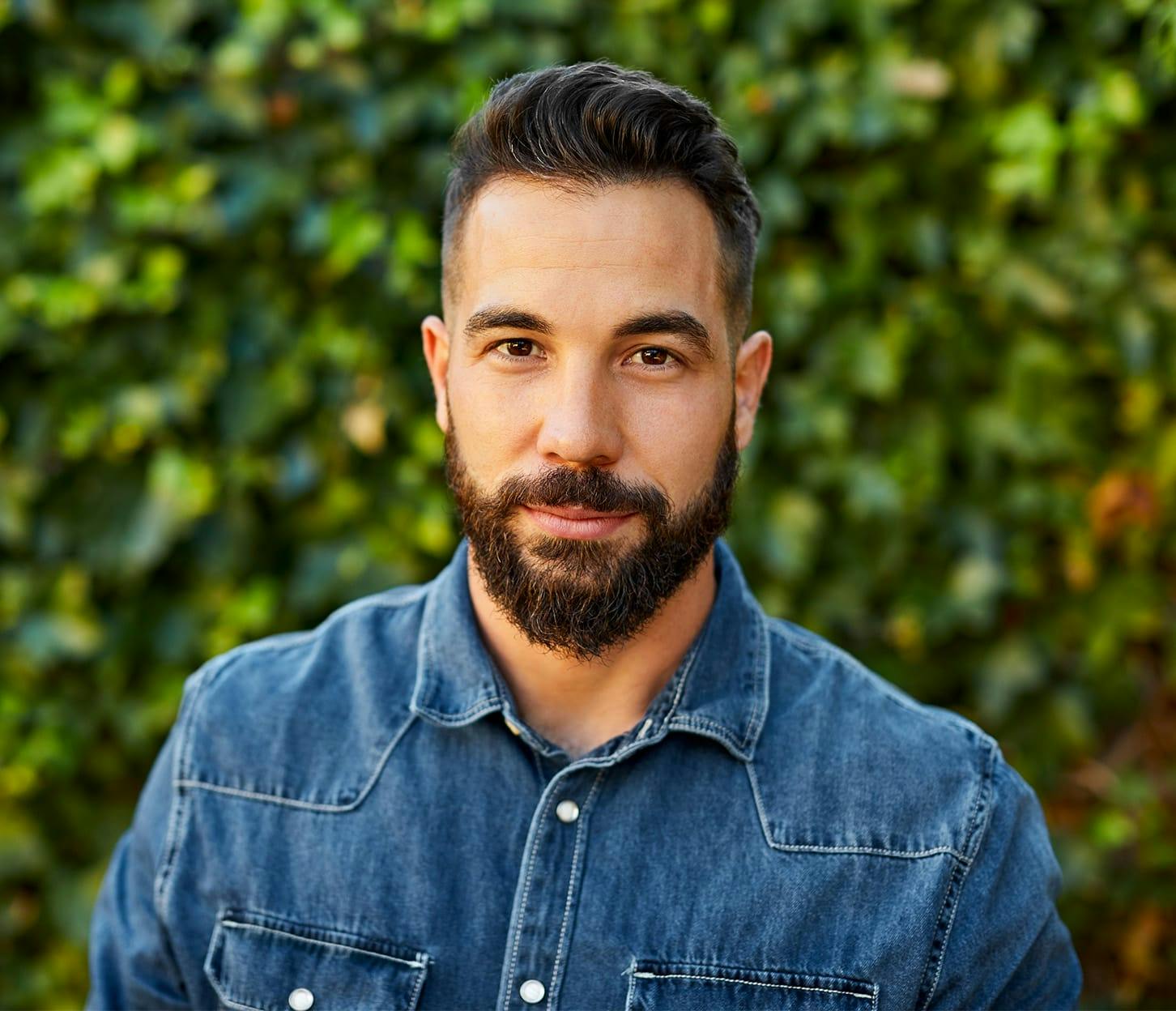 man in jean jacket in front of wall of vines