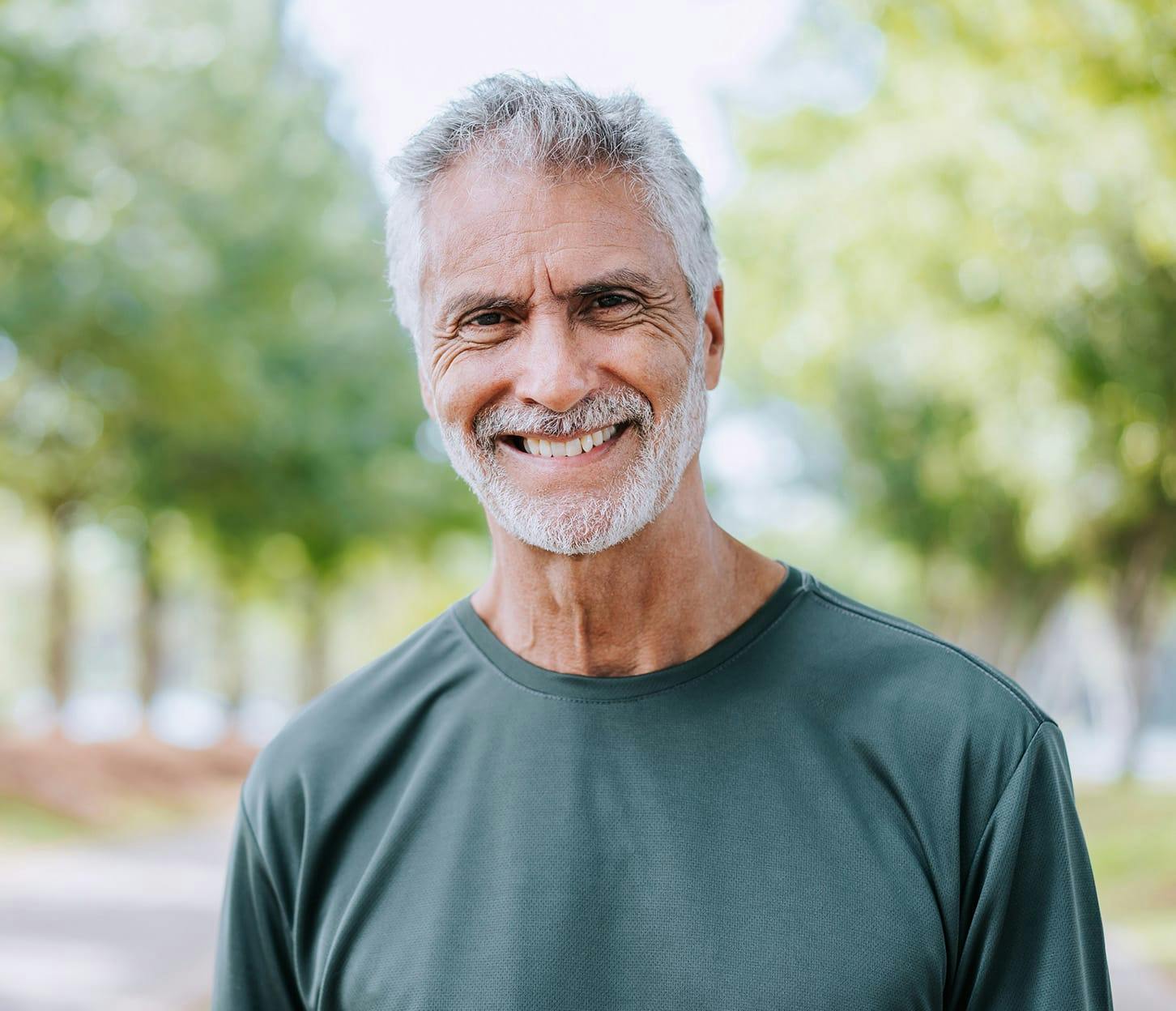 older man smiling with trees behind him