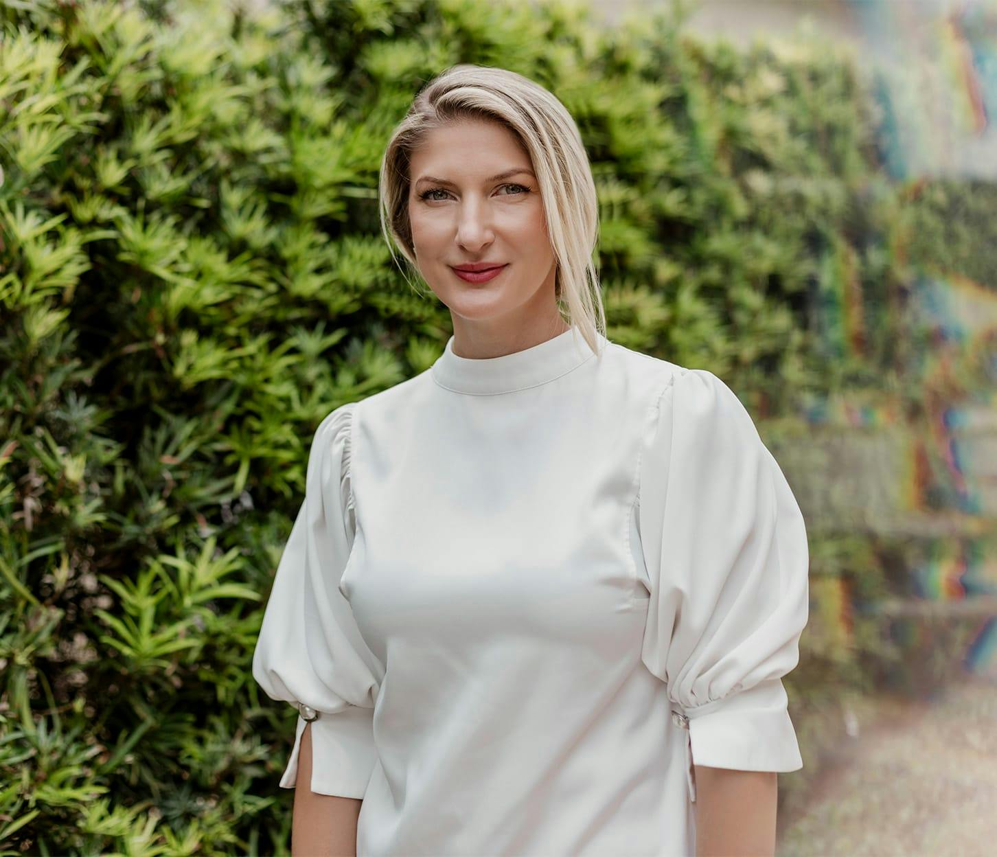 Dr. Quimby in white top standing in front of hedges