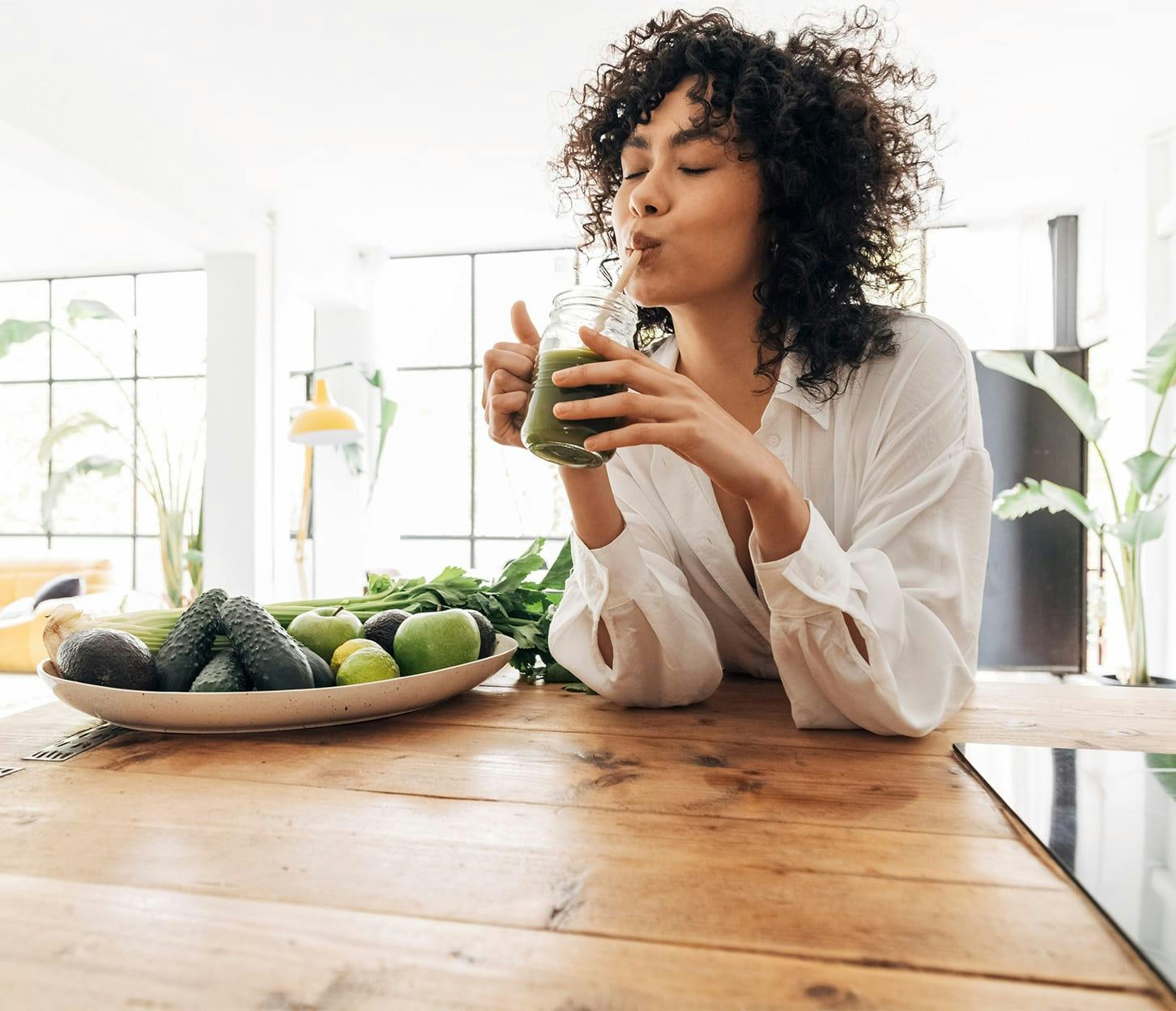 woman with big curly hair drinking green smoothie