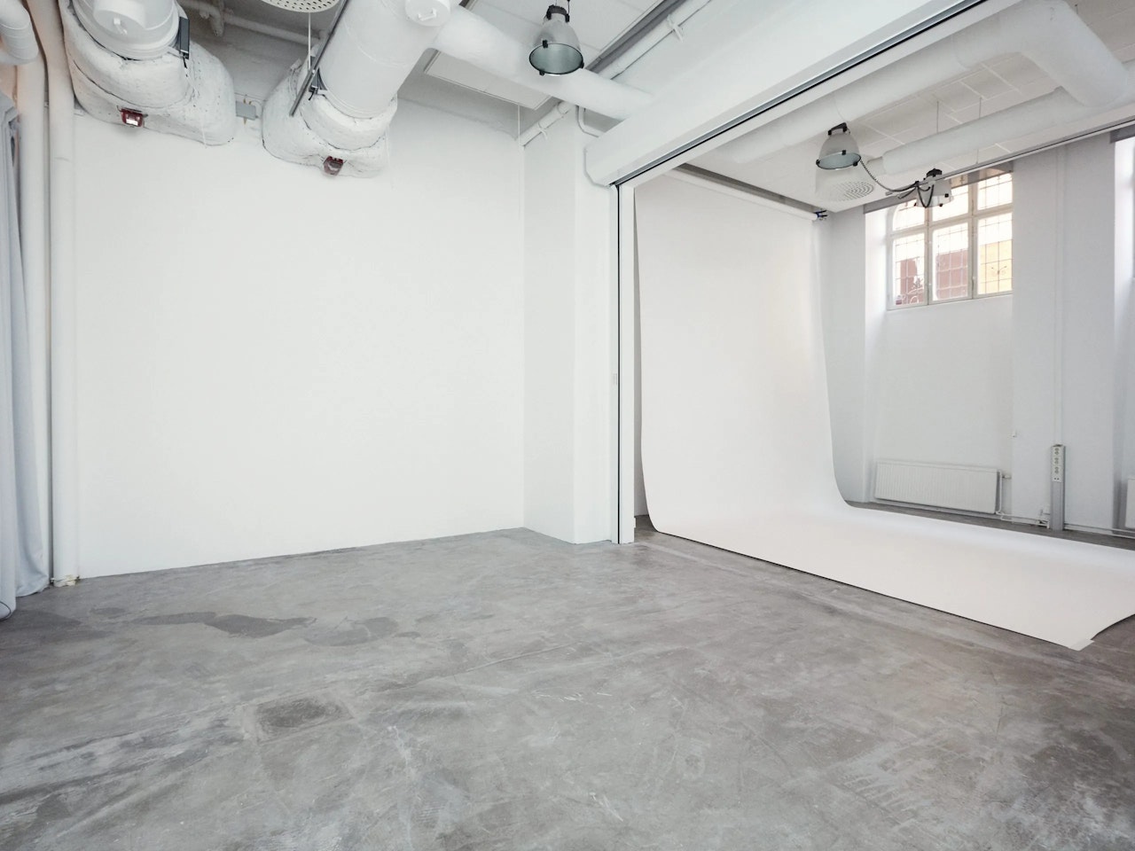 Spacious, empty photo studio with white walls, concrete floor, and backdrop.