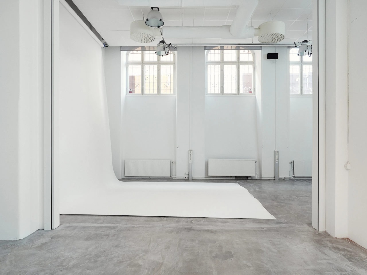 Photography studio with a white backdrop, large windows, and concrete floor.