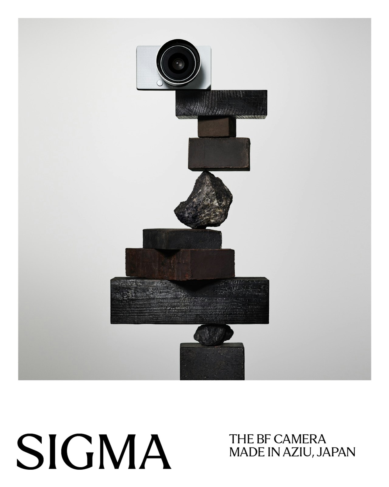 A Sigma camera balances atop stacked rocks and wooden blocks against a plain background.