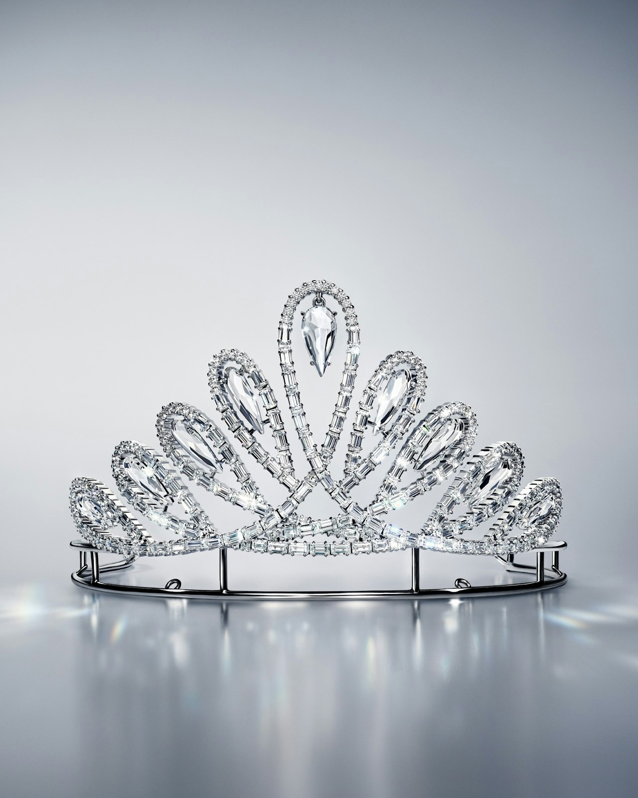A sparkling silver tiara with teardrop-shaped crystal details on a reflective surface.